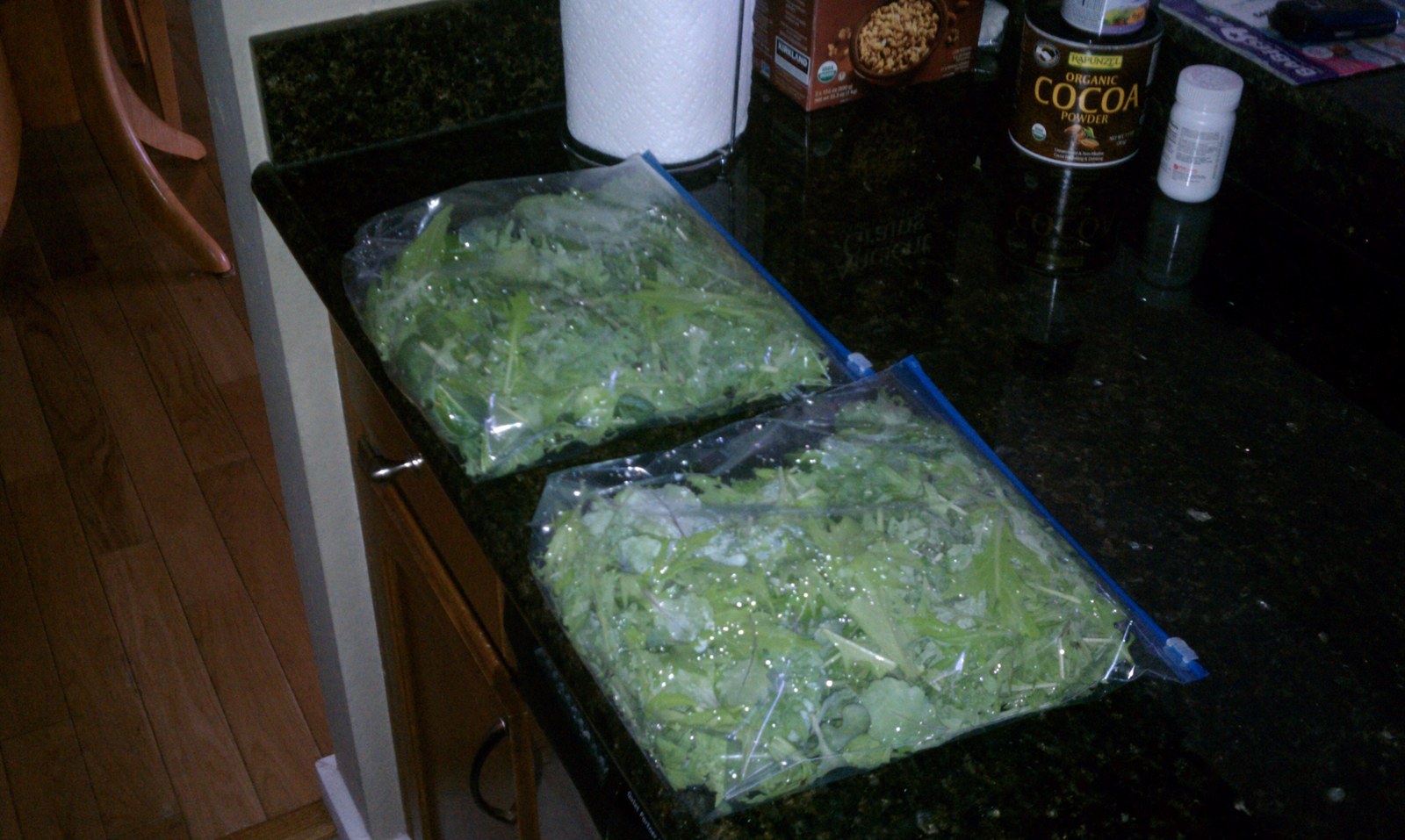 Two large zip bags packed full of washed salad greens lying on the kitchen counter.