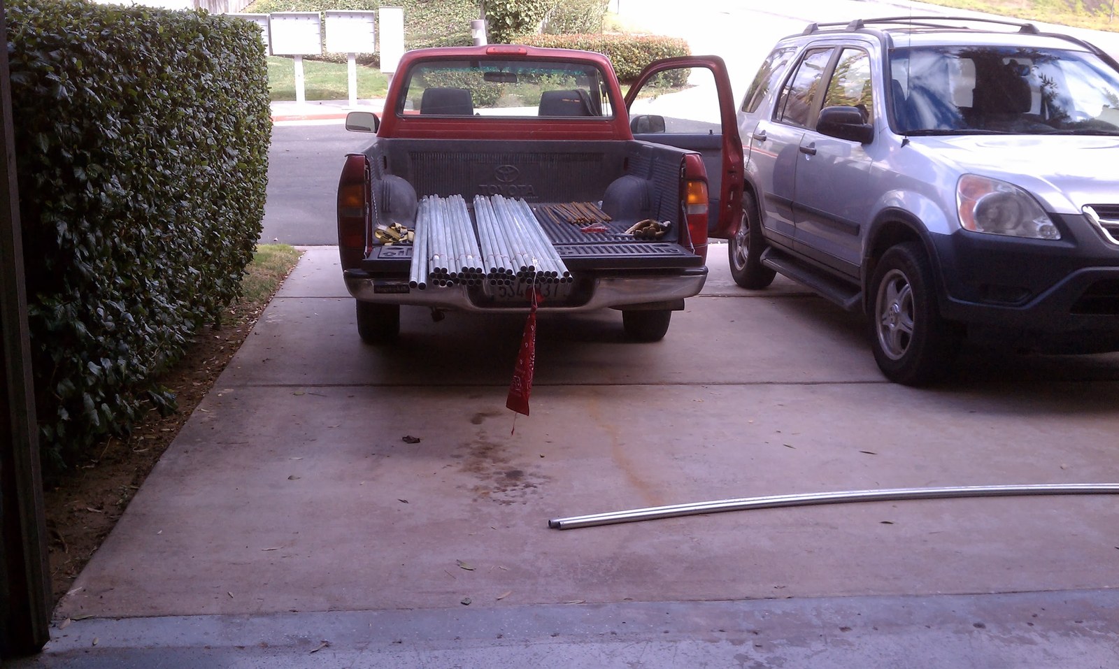 A pickup truck in a driveway with its bed loaded with straight metal conduit.