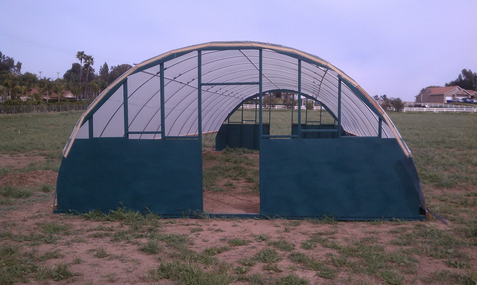 The completed hoop house with finished green end walls and a center door.