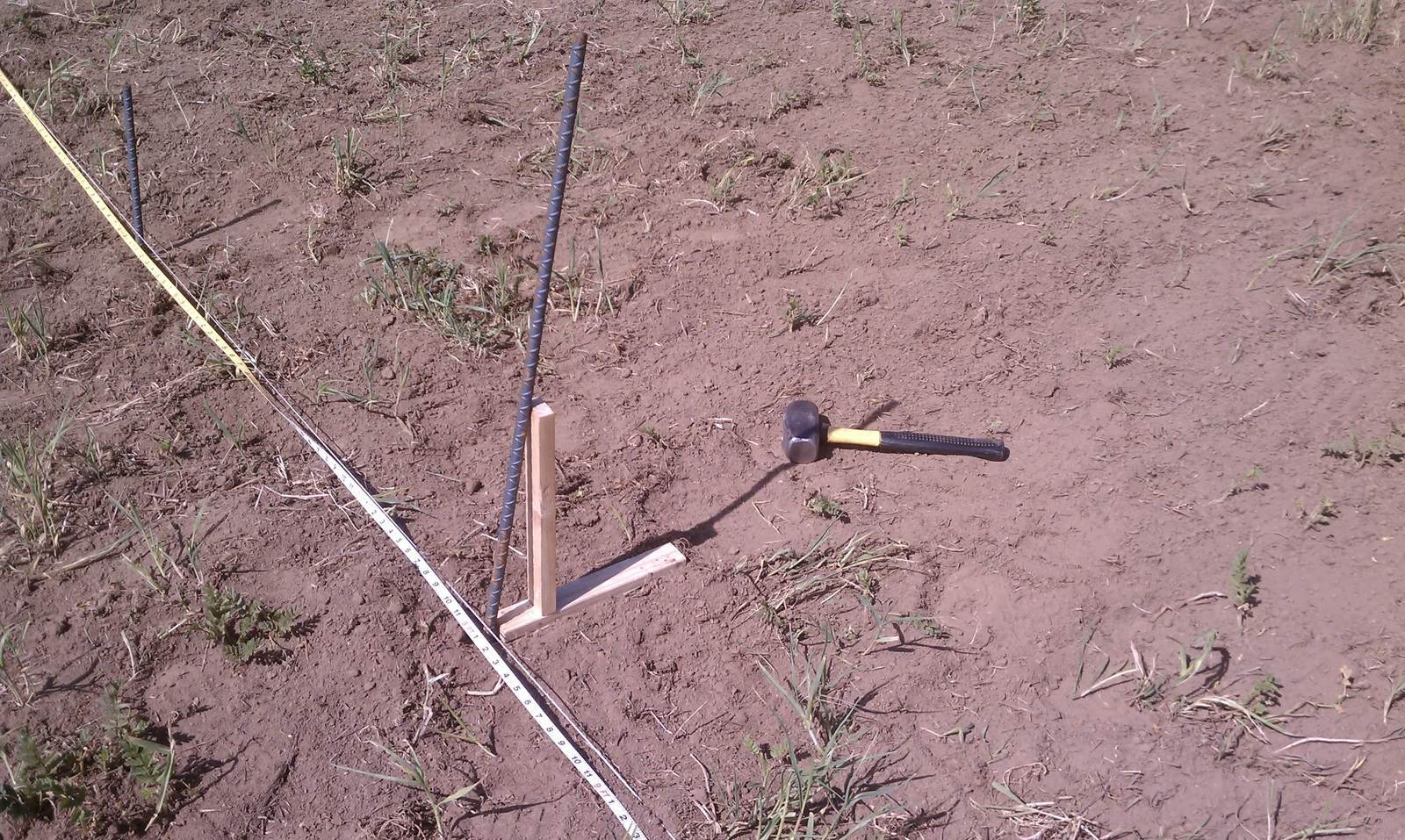 A tape measure, hammer, and stakes marking a line on the bare dirt.