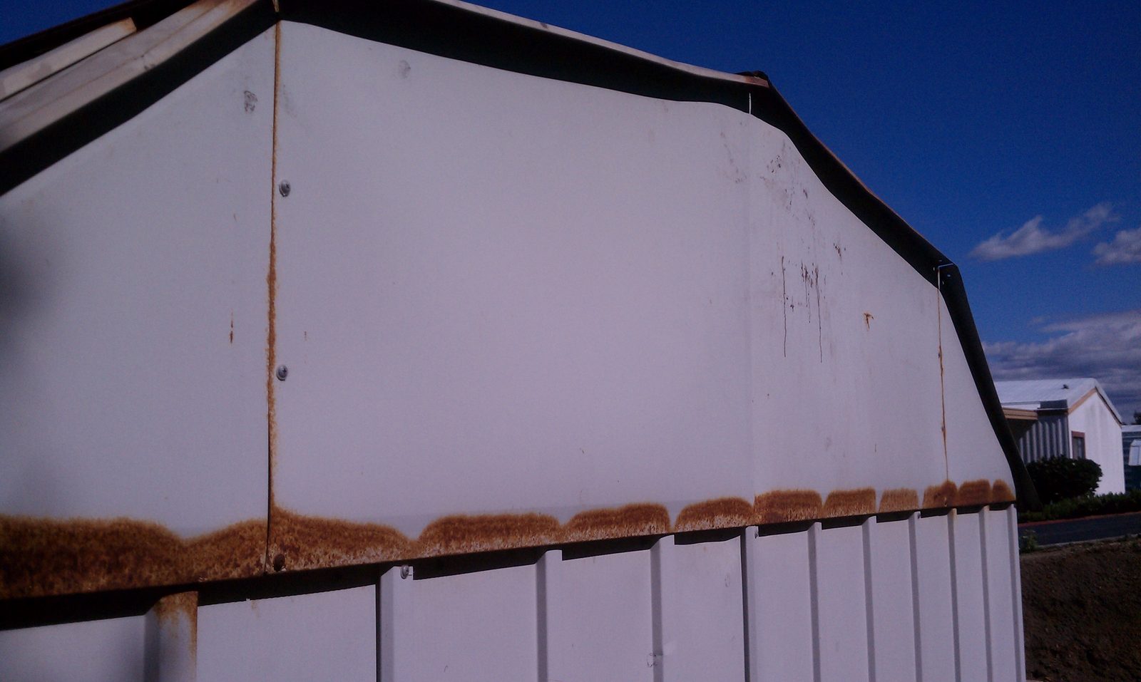 The white metal garden shed at its original home, rust running along the roof seams.