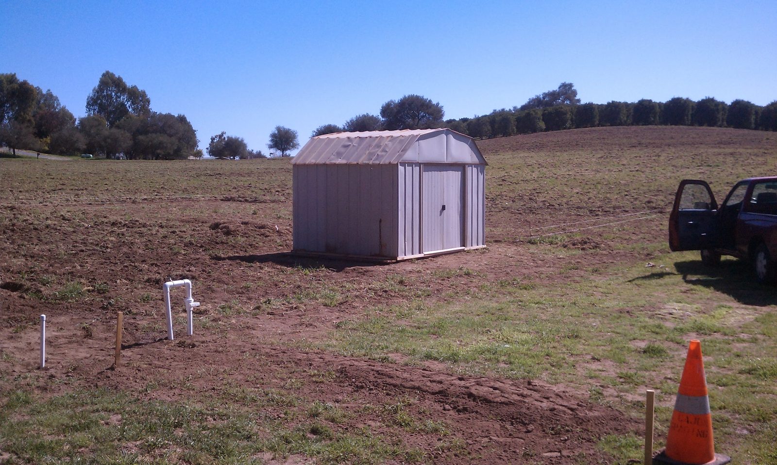 The reassembled shed standing on the field with the truck beside it and the new spigot riser in the foreground.