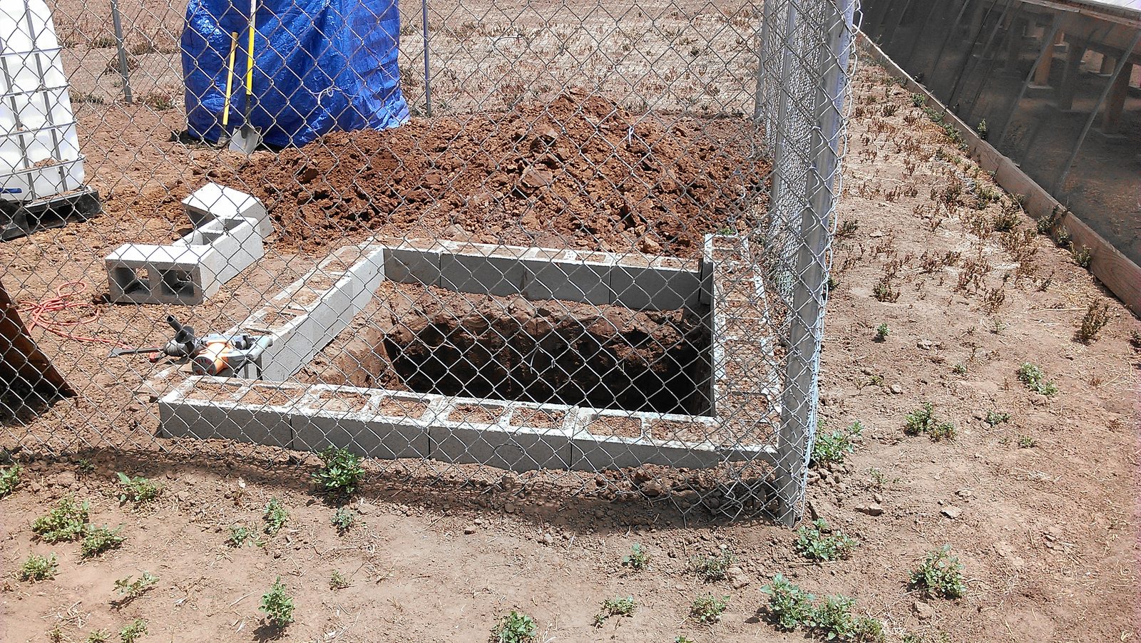 The first courses of concrete block laid around the sump pit, spoil heaped behind.