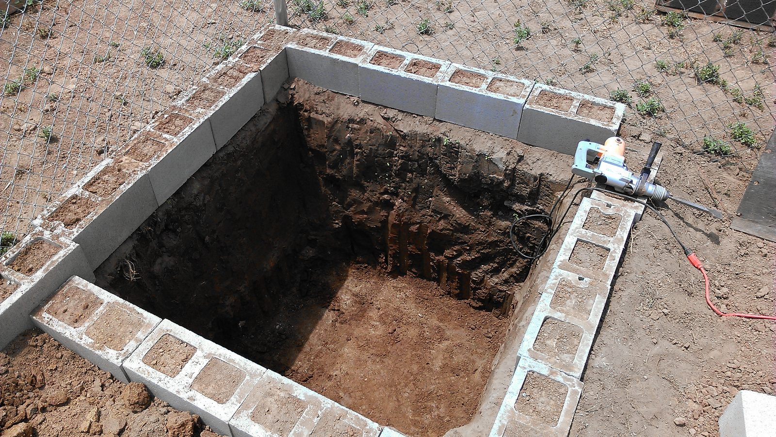 The pit cut square and deep inside the block ring, a small pump and cord at its edge.