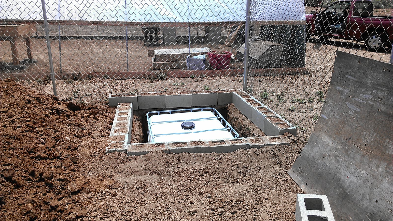 The tote sitting in the block-lined pit seen from a few steps back, fence and shed behind.