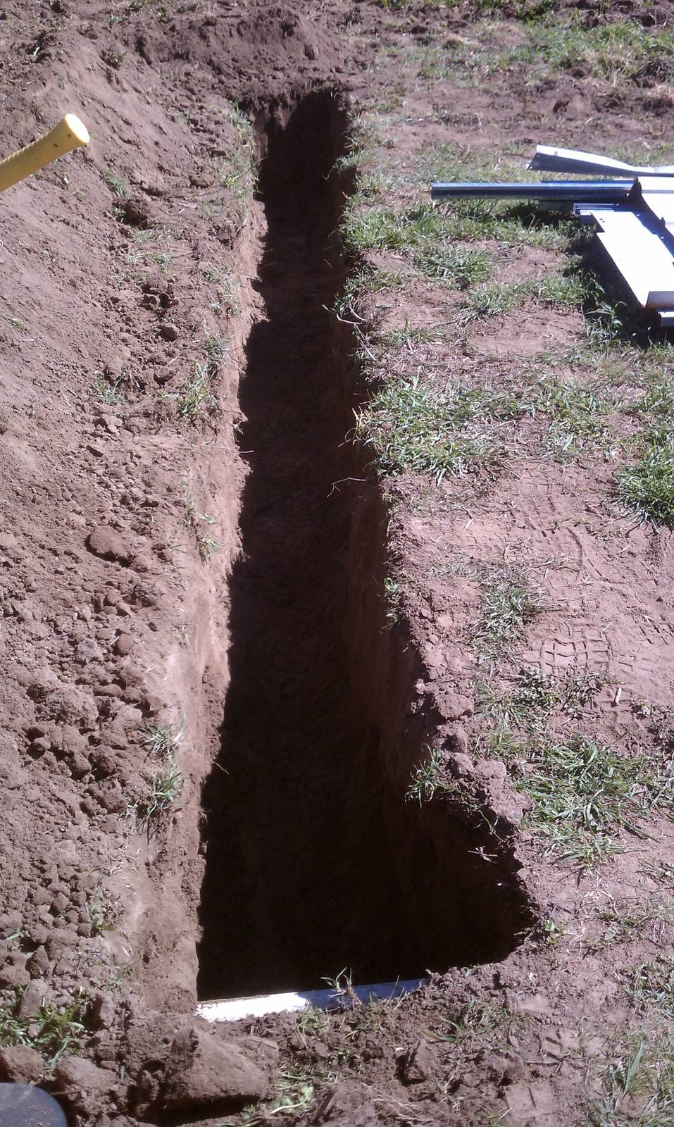 Looking straight down the length of a narrow, freshly dug trench.