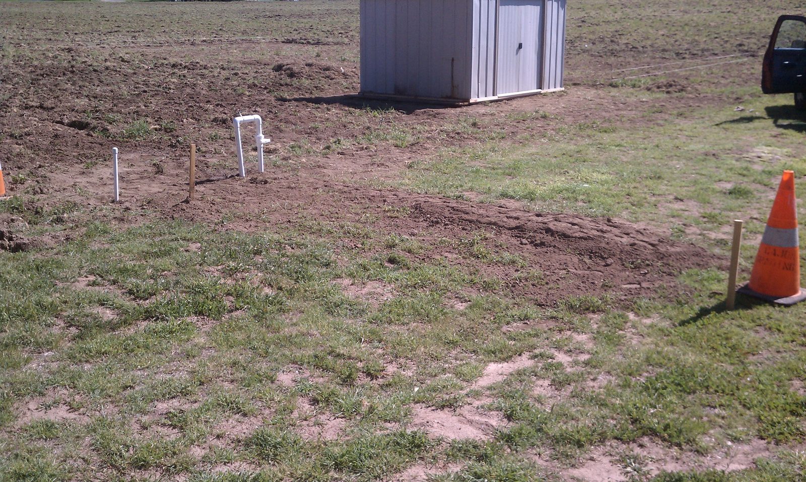 A finished standpipe and spigot in the open field with the shed behind it.