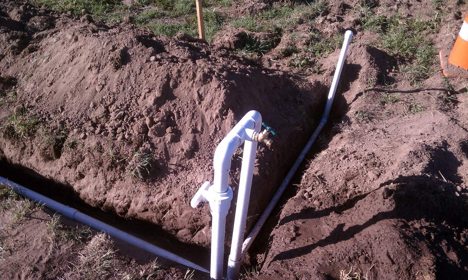White PVC fittings joining the riser to the buried supply line.